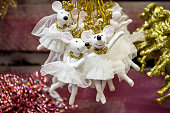 Christmas toys in the form of mice-ballerinas in white tutus, gold crowns, dancing in pairs, as if they had a ball. Blurred pink background with shiny Christmas decorations and branches