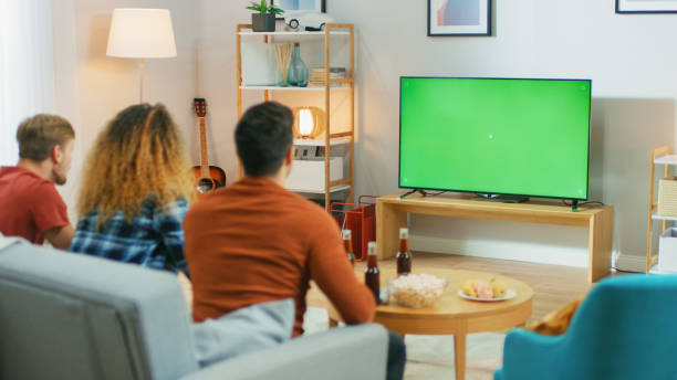 istock Three Friends Sitting on a Couch at Home, Watch Green Chroma Key Screen TV while Eating Snacks and Drinking Beverage. Young People Having Fun at Home. 1178291781