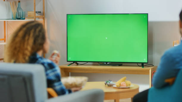 coppia felice seduta a casa nel soggiorno a guardare la tv con chiave chroma verde, rilassarsi su un divano. coppia camera guardare partita sportiva, notizie, spettacolo o un film. - home movie foto e immagini stock