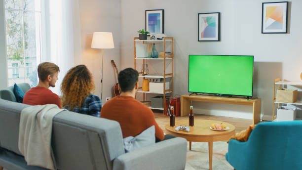 istock Three Friends Sitting on a Couch at Home, Watch Green Chroma Key Screen TV while Eating Snacks and Drinking Beverage. Young People Having Fun at Home. 1178291805