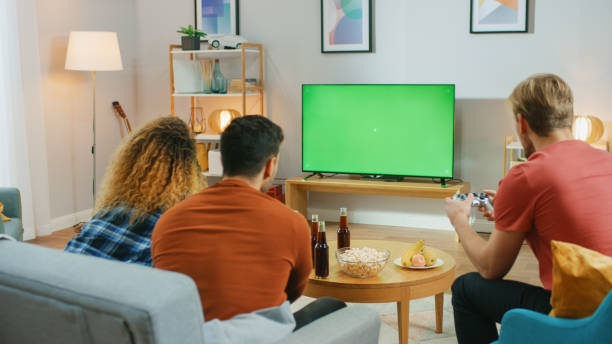 w salonie trzech przyjaciół konkurencyjnie grać w gry wideo na green chroma ekran klucza, za pomocą kontrolerów. nastolatki bawiące się w domu. - friendship video game young adult party zdjęcia i obrazy z banku zdjęć