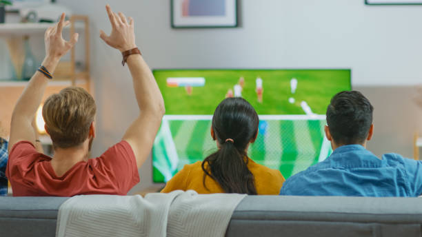 in home diverse group of sports fans sitting on a couch watching important soccer game on tv, they cheer for the team, celebrate victory after team scoring winning winning goal. freunde hugging. - watching the game fotos stock-fotos und bilder
