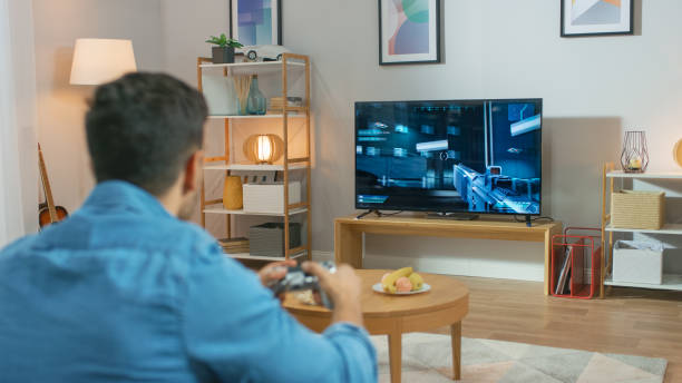 istock In the Living Room Man Sitting on a Couch Holds Controller Playing in a Console Video Game, 3D Action Shooter Gameplay Shown on TV Screen. 1178291900