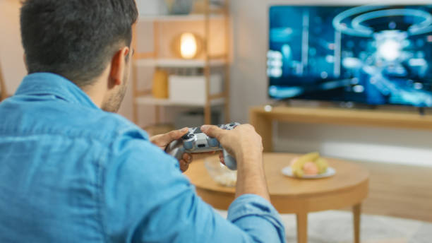 istock In the Living Room Man Sitting on a Couch Holds Controller Playing in a Console Video Game, 3D Action Shooter Gameplay Shown on TV Screen. 1178292335