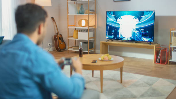 istock In the Living Room Man Sitting on a Couch Holds Controller Playing in a Console Video Game, 3D Action Shooter Gameplay Shown on TV Screen. 1178292436