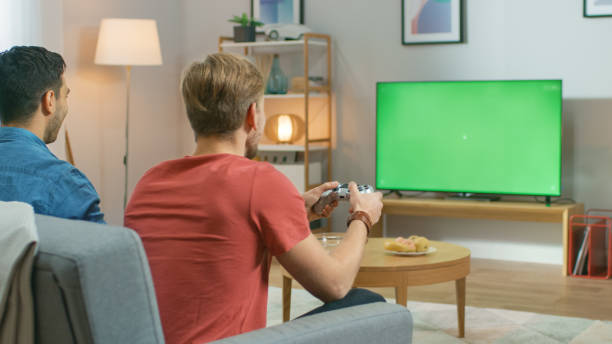 istock In the Living Room Two Friends Sitting on a Couch Holding Controllers Playing Competitive Video Game on a Green Chroma Key TV Screen. 1178292437