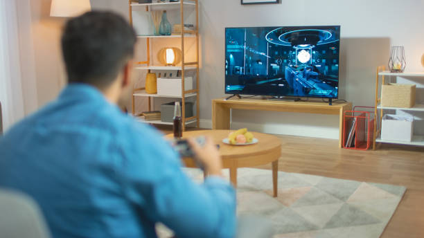 istock In the Living Room Man Sitting on a Couch Holds Controller Playing in a Console Video Game, 3D Action Shooter Gameplay Shown on TV Screen. 1178292522