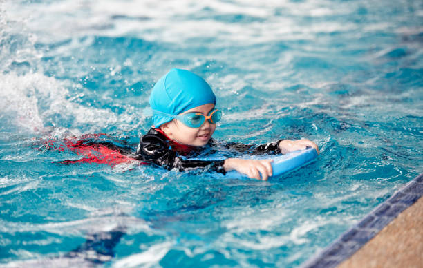 One girl wearing practice swimming. One girl wearing a swimsuit uses a foam pad to practice swimming in a swimming pool with a teacher. She happily and smiling. asian kids learning stock pictures, royalty-free photos & images