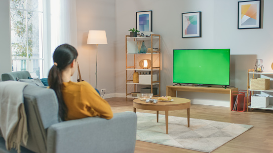 Girl Sitting At Home Sitting on a Couch, Watching Green Chroma Key Screen, Relaxing. Man in a Cozy Room Watching Sports Match, News, Sitcom TV Show or a Movie.