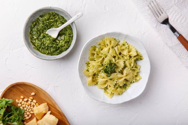 Farfalle pasta in  basil pesto sauce in white plate on white table. Top view.