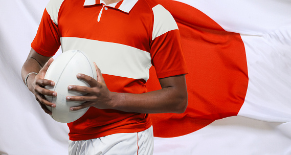 Male rugby player with a ball in front of a Japanese flag