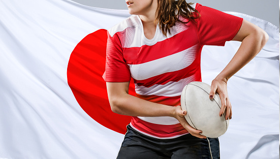 Female rugby player with a ball in front of a Japanese flag