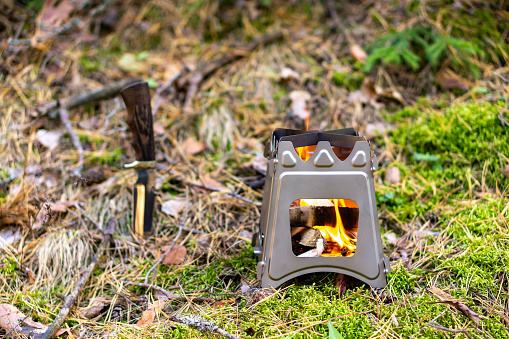 Burning foldable wood stove designed for cooking outdoors using twigs as fuel on nature background