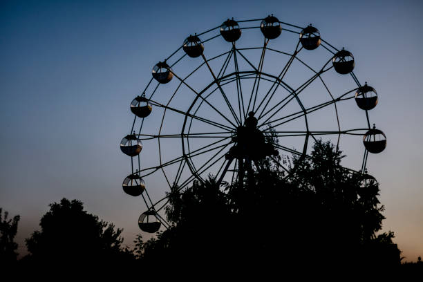 Silhouette of a ferris wheel at sunrise (sunset) of the sun on a background of trees and grass. Silhouette of a ferris wheel at sunrise (sunset) of the sun on a background of trees and grass. Beautiful background with copy space. abandoned roller coaster stock pictures, royalty-free photos & images