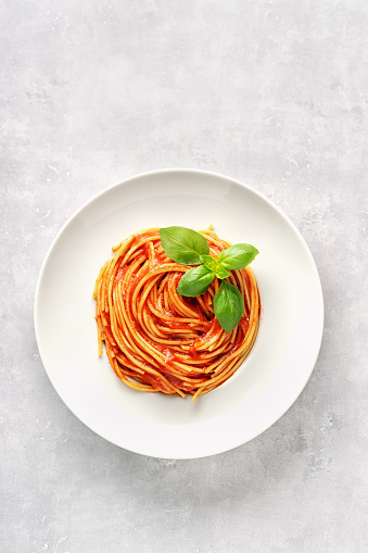 Pasta with tomato sauce and basil on white background. Vertical shot