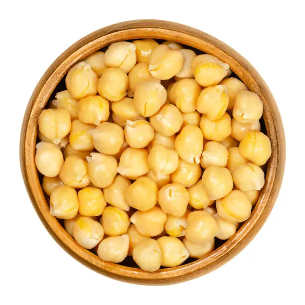 Cooked chickpeas in wooden bowl. Light tan Kabuli chickpea variety. Chick peas, Cicer arietinum, high protein legume and ingredient of hummus. Closeup from above on white background, macro food photo.