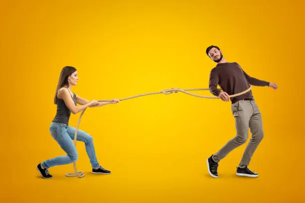 Side view of young woman lassooing young man on yellow background. Predator - prey relationship. Emotional immaturity. Rush into marriage.