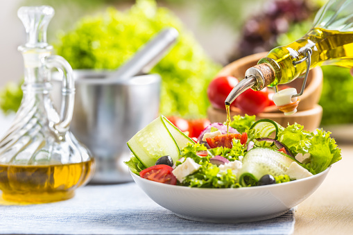 Olive oil pouring in to the fresh vegetable salad. Healthy mediterranean italian or greek cuisine.