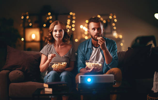 familienpaar schaut tv-projektor zu hause auf sofa - family sofa men sitting stock-fotos und bilder