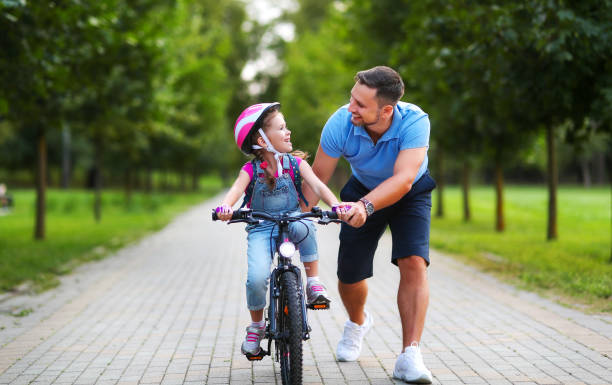 幸せな家族の父親は、公園で自転車に乗るために子供の娘を教えます - park and ride ストックフォトと画像