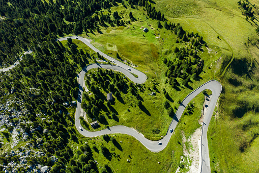 Aerial view of an alpine road surrounded by Italian alps and pine forest.