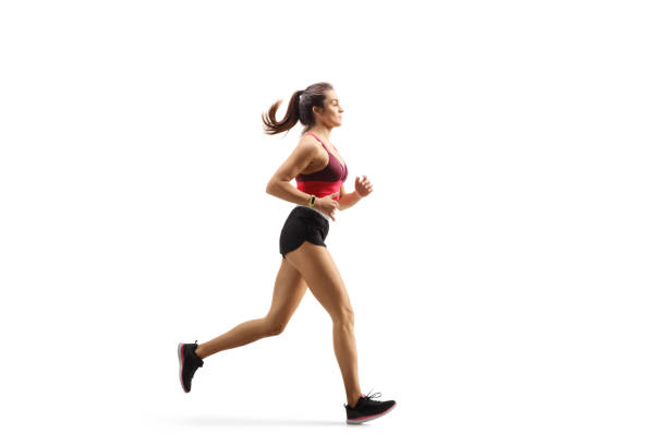 Young female athlete in sportswear jogging Full length profile shot of a young female athlete in sportswear jogging isolated on white background running shorts stock pictures, royalty-free photos & images