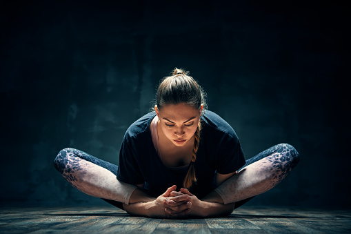 Young woman practicing yoga doing reclined goddess pose asana in dark room. Supta Baddha Konasana. Wellness and healthy lifestyle