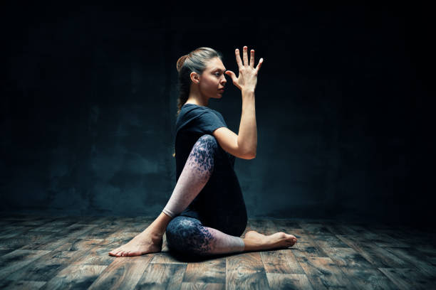 Young beautiful woman doing yoga asana half lord of the fishes pose on dark room Young beautiful woman doing yoga asana half lord of the fishes pose on dark room. Practicing yoga, wellbeing and healthy lifestyle. Ardha Matsyendrasana twist pose stock pictures, royalty-free photos & images