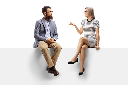 Full length shot of a young woman having a conversation with a bearded man while sitting on a panel isolated on white background