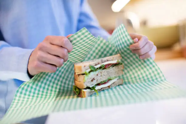 Photo of Close Up Of Woman Wrapping Sandwich In Reusable Environmentally Friendly Beeswax Wrap