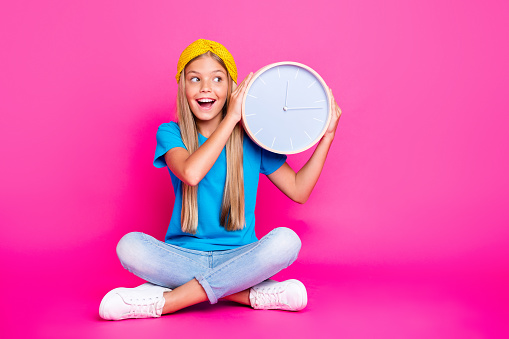 Tick tock. Portrait of funny funky kid hold clock listen to minutes seconds wait for her birthday, party leisure holidays wear blue t-shirt denim jeans sneakers isolated over bright color background