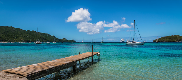 Seascape with luxury sailboats, boats and cruise ship. Wooden pier at a white sandy beach of Bequia, St Vincent and the Grenadines. Blue sky and white clouds on a beautiful sunny day. Port Elisabeth in the background.