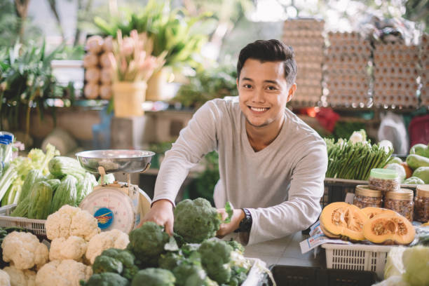 un propriétaire asiatique malay légumes au détail organiser ses légumes se préparer pour l'entreprise en regardant la caméra - business malaysia photos et images de collection