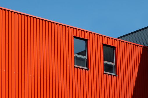 Part of the facade of a red warehouse building with two windows against a blue sky. The concept of renting or selling premises for a shop, workshop, hangar, garage, car service. Commercial property.