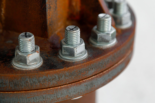 New galvanized bolts connect old rusty metal parts close-up on a light blurry background. The symbol of the unification of the large through the many smalls.