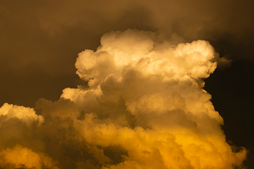 Close-up sky with cumulonimbus cloud at sunset, reflecting vivid colors.