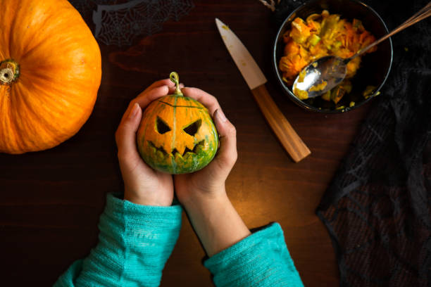 Photo of hands holding jack-o-lantern from pumpkin sitting at wooden table