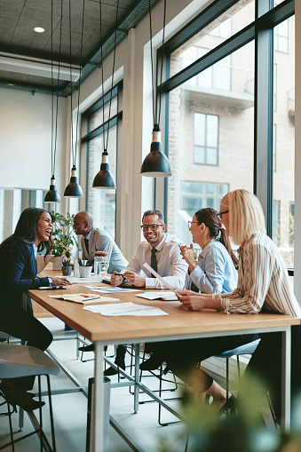 Smiling group of diverse businesspeople going over paperwork together during a meeting around a table in a modern office