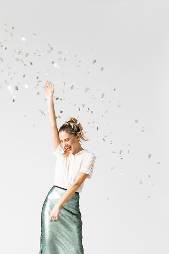 Studio shot of beautiful elegant smiling young woman dancing under confetti.
