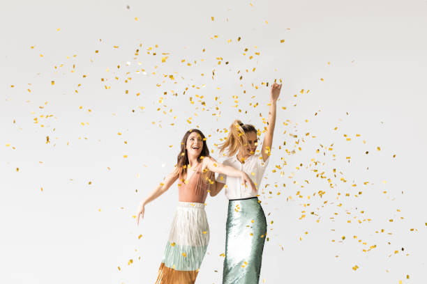 Party Girls Dancing Under Confetti Studio shot of two beautiful stylish young women smiling and dancing under confetti. anniversary photos stock pictures, royalty-free photos & images