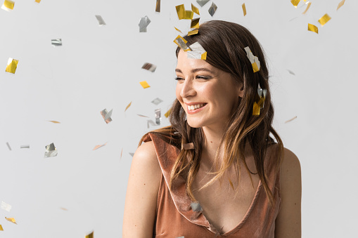 Studio shot of beautiful young smiling woman feeling happy under confetti.