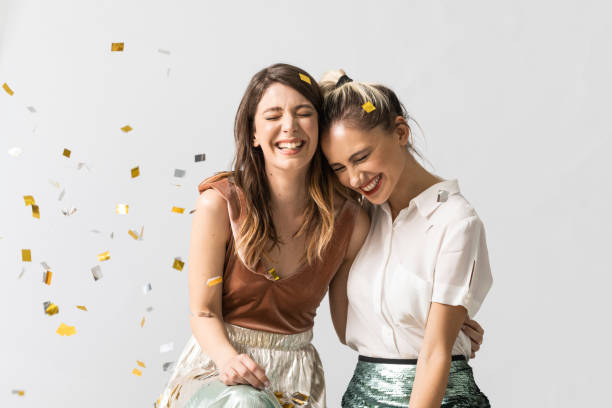 Portrait of Girlfriends at the Party Portrait of two beautiful laughing young women hugging and celebrating under confetti. two people embracing stock pictures, royalty-free photos & images