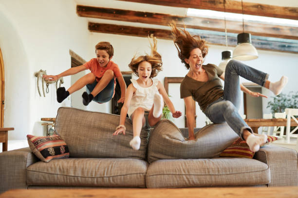 gareggia per il posto migliore sul divano. madre e figli che saltano. - family cheerful happiness domestic life foto e immagini stock