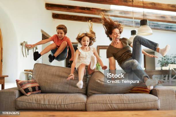 Race For The Best Spot On The Sofa Mother And Children Jumping Stock Photo - Download Image Now