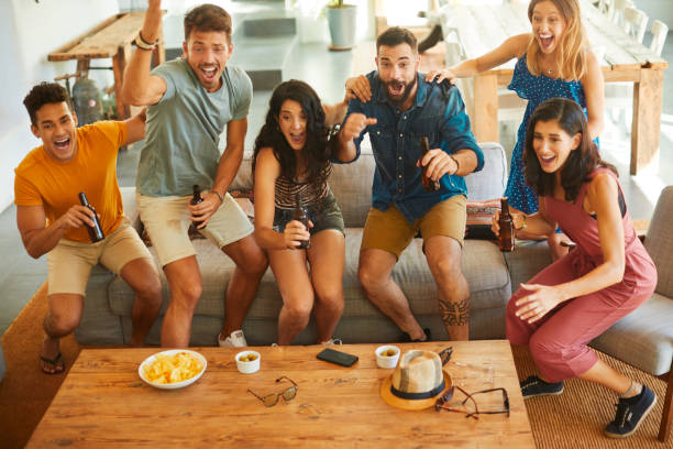 Group of friends jump in joy when their team scores a goal. Friends enjoying time together and partying in a Spanish home. cheering photos stock pictures, royalty-free photos & images
