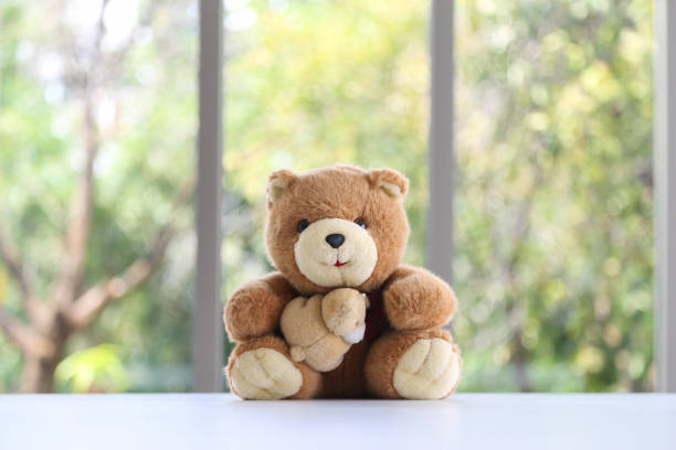 A cute teddy bear with mini bead doll on white table with nature background outside window.