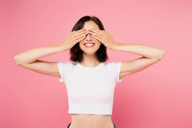 bella ragazza sorridente con le mani sugli occhi isolati sul rosa - hands covering eyes foto e immagini stock