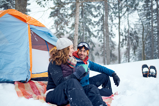 Diverse couple of indian guy and caucasian woman setting camp with a tent in a snow filles canadian park during a snowshoeing trip