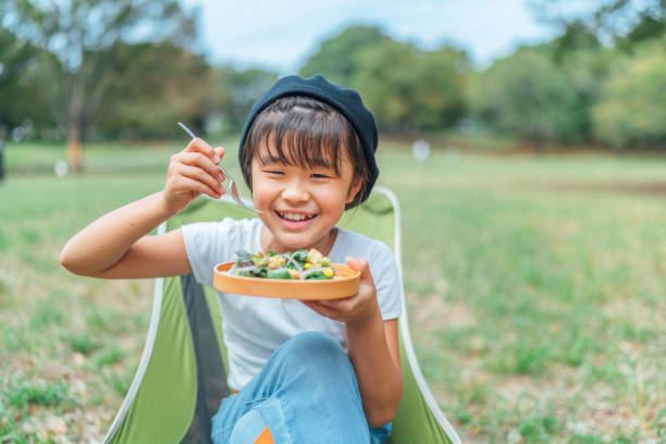 Small girl eating vegan food outdoors A small girl is eating vegan food in a public park happily.
She is eating corns, beans, arugula, onion. child japanese culture japan asian ethnicity stock pictures, royalty-free photos & images