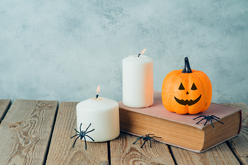 Halloween holiday concept with  jack o lantern glitter pumpkin decor, old book and candles on wooden table